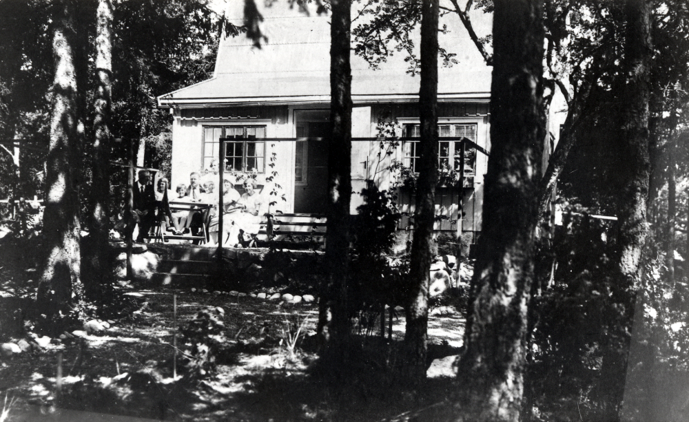 Familjen Gumaelius samlad på verandan till sitt sommarställe Gumaeliebo. På annat ställe nämns att huset kallades Sturehof. Huset revs 1965. På dess plats ligger Fornminnesvägen 30-32. På verandan sitter fr v Johan Bernhard Gumaelius, Elly Gumaelius gift Forss, Inga Gumaelius, Eric Gumaelius, Birgit Gumaelius gift Sundman, Ingeborg Gumaelius gift Stennemark, Anna Gumaelius och Dagny Gumaelius. Anna och Eric är föräldrar till de fem flickorna