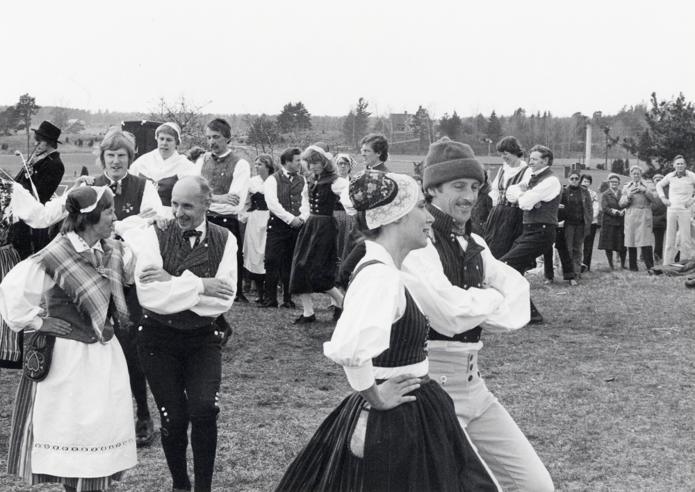 Vallentuna folkdansförening dansar i samband med ett besök från Säters folkdanslag i slutet av 1970-talet.  Främst dansar Eva och Sigge Rahmqvist, sedan fyra par från Säter och t h om Sigges mössa Ingrid Rost och Alf Olsson.  Bakom dansarna syns t h taket på Kvarnbadet och i bakgrunden Villa Kullen
