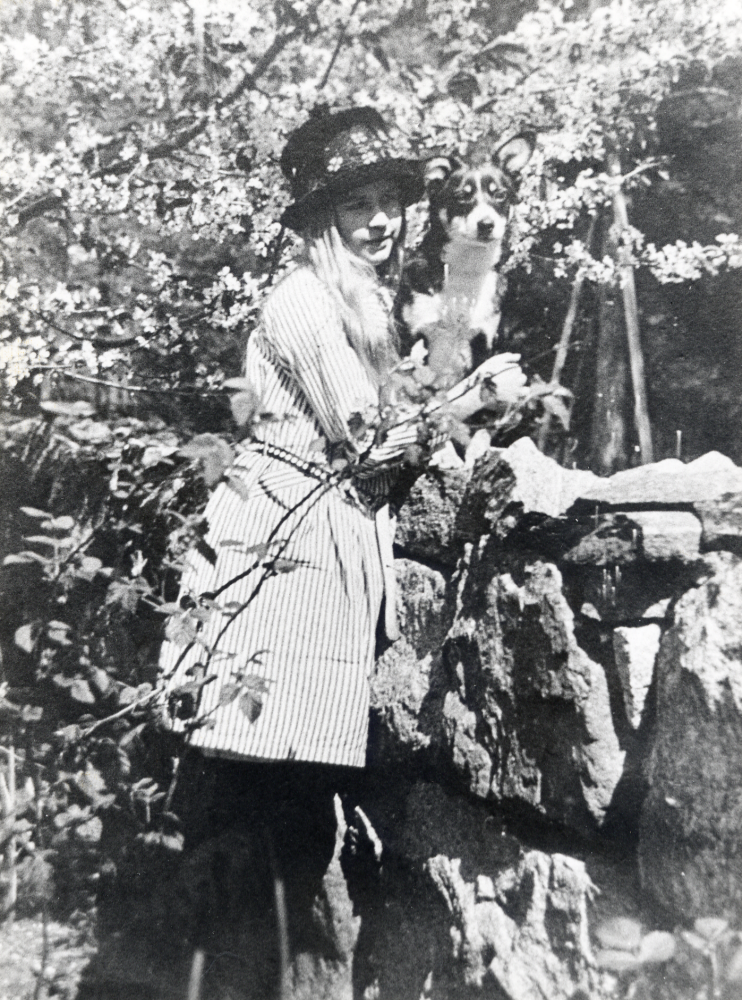 Gertie Börjesson gift Dethorey med hunden Pejk. Fotot taget av okänd fotograf stenmuren till Lillbo i Vallentuna. Fastigheten brann ner till grunden 1954, den var byggs 1907 av bokhandlare Karl Börjesson Gerties far