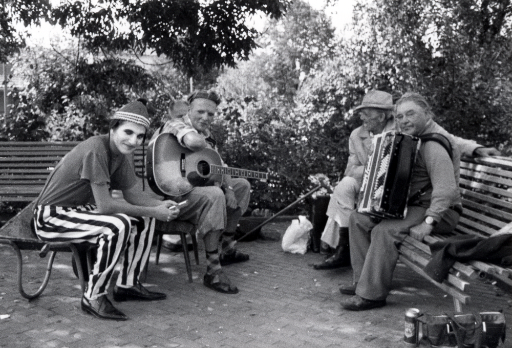Gycklarna Magnus Andersson i randiga byxor och Per Norbäck med gitarr i samspråk med Helmer Eriksson med dragspel och okänd vid sofforna på Tuna torg i samband med Vallentuna marknad