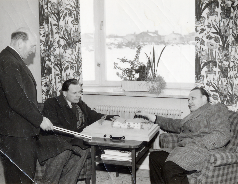Bröderna Nils Jorild och Harry Jorild samtalar med kommunalnämndens ordförande Gustav Nilsson. Framför sig har de en husmodell