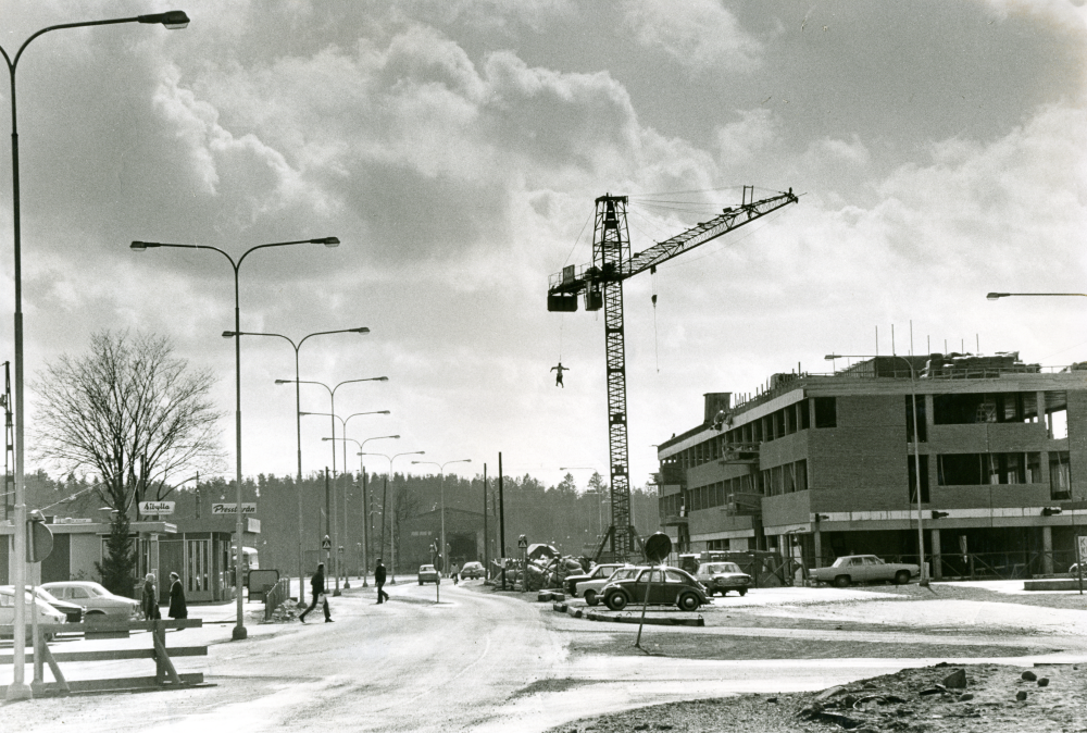 Jobbarna på bygget av Tunahuset har hängt upp en docka i lyftkranen i protest mot att de inte skulle få anordna taklagsfest. Dockan byttes sedan ut mot en krans, som visade att byggnadsarbetarna skulle få sin taklagsfest. 
•Fotografiet ingår i bildserien ”Vardagsliv i Vallentuna kommun” av Rachael Gough-Azmier & Gunilla Blomé, Haga Studios HB.
