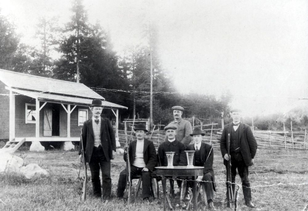 Medlemmar i Vallentuna skytteförening samlade utanför gamla paviljongen vid Fågelsången. Längst till vänster står Ferdinand Lindström och i mitten vid bordet sitter Carl Bornholm.  På bordet står två pokaler