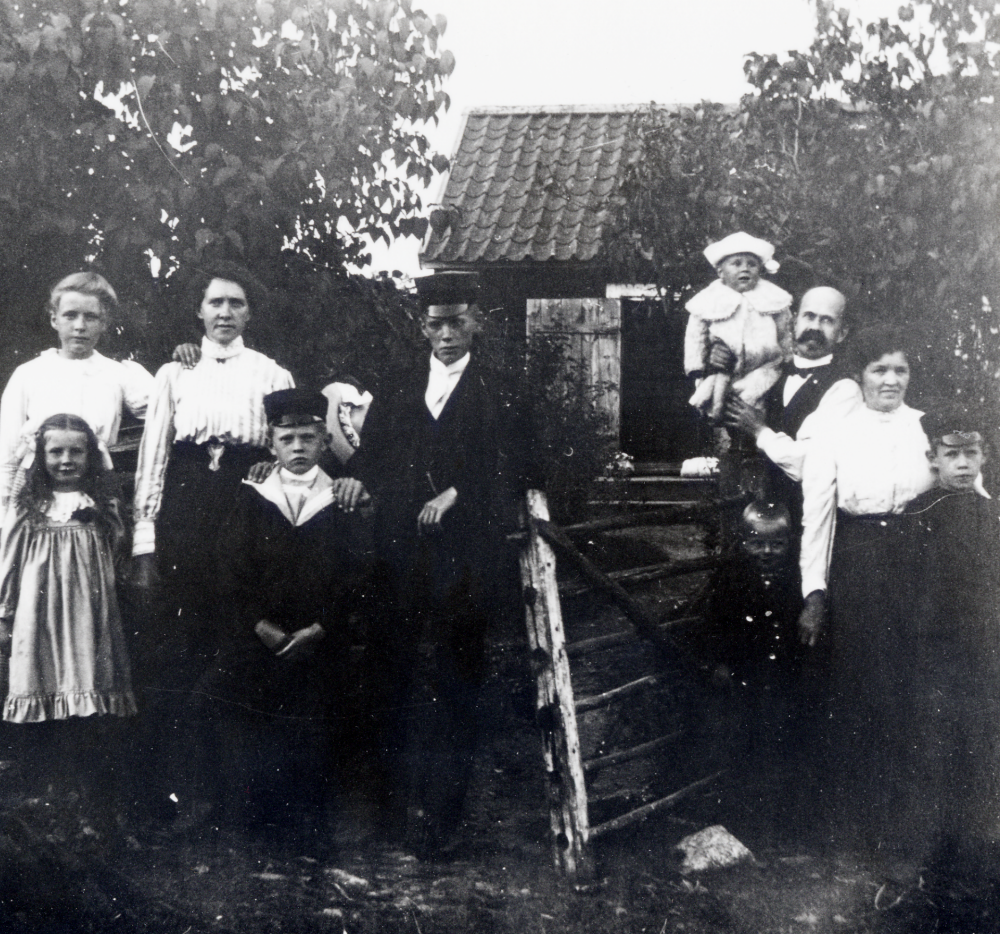 Familjebild utanför Björkedal vid Lingsberg i Vallentuna.  Familjen Brunnberg med släktingar hyrde Björkedal och gamla småskolan i Lingsberg, som senare fick namnet Björkhaga, som sommarställe.  Björkedal låg öster om Björkhaga.  Fr v står okänd samt okänd liten flicka, Matilda Brunnberg, pojkarna i skärmmössor okända, Olof Olsson med sonen Filip på armen född 1905 samt hustrun Edla.  Pojken framför Edla är ev fostersonen Gösta