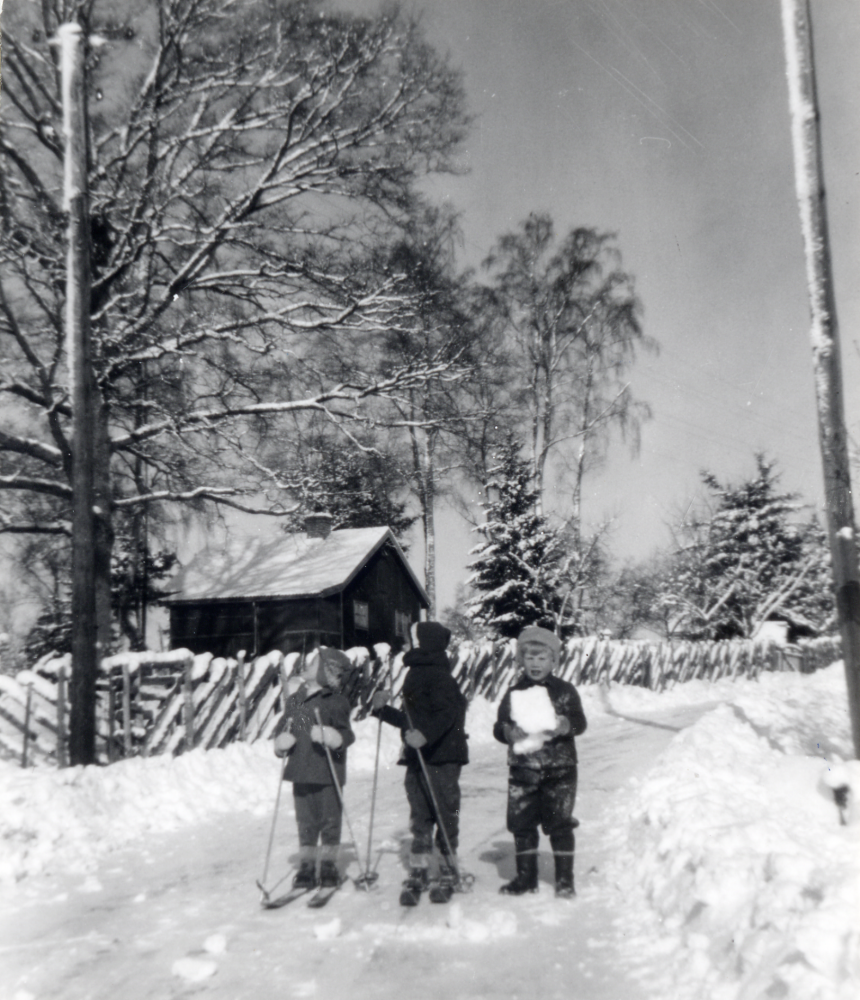 Vinterväg utanför sommarstugan Hasselbacken vid Wasavägen, Djurgården i Lindholmen. Stugan ägdes av Eric Holmberg med familj. 
Barnen, två på skidor fr v Per-Anders Karlsson, Annika Ahlsén och Lars Ståhl med en snökoka i famnen. Alla barnen bodde vid Wasavägen.