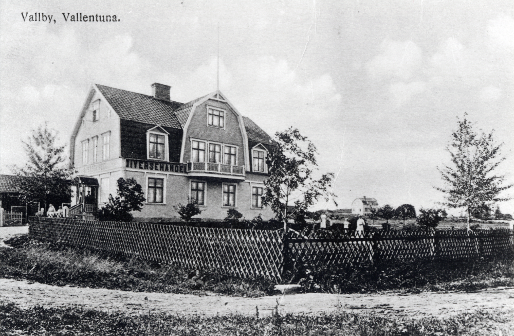 Vallentunas största specerihandel har haft flera ägare.  Conrad Österberg  byggde affären 1907-08. Den kallades  Vallby.  1920 övertogs rörelsen av  Valfrid Jansson  som 1934 sålde den till  Erik L Andersson.  1938 köptes affären av  Georg Tibell  som drev affärsrörelse fram till början av 1960-talet.  Fastigheten revs 1962.  På dess plats uppfördes en ny  Konsumhall  invigt 1965.
Se Lanthandlare i vallentunasocknarna vid Roslagsbanan