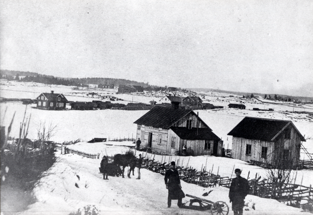 Vy över Vallentuna från  Skolvägen Fattistubacken.  En man med  skottkärra  och en  häst  med  släde  står i backen. I huset  t v fanns affärslokaler, vilka bl a hade följande innehavare:  Erik Halvarsson,  Lisa Edman  och  Konsum.  Huset längst ner t h mot järnvägen innehade bl a en  telefonstation   Huset  brann 1911. Bakom affärslokalen syns  Vallentuna järnvägsstation  och  järnvägsrestaurant   I  bakgrunden syns  Rickebyhöjd  och  Rickeby gård