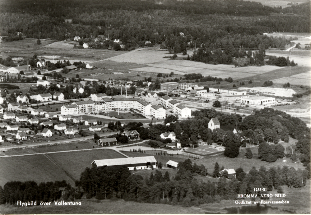 Flygfoto över Vallentuna centrala delar. I förgrunden Vallentuna kyrka med Prästgården och dess ekonomibyggnader. I bildens mitt Vallentuna centrum, Tellus Maskin och t v Vallentuna tegelbruk