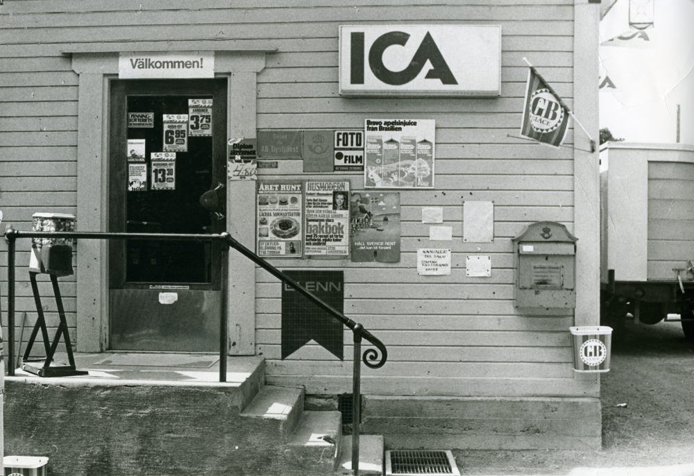 Ica-butiken i Lindholmen. Brevlåda, reklamskyltar och löpsedlar på fasaden.
•Fotografiet ingår i bildserien ”Vardagsliv i Vallentuna kommun” av Rachael Gough-Azmier & Gunilla Blomé, Haga Studios HB.