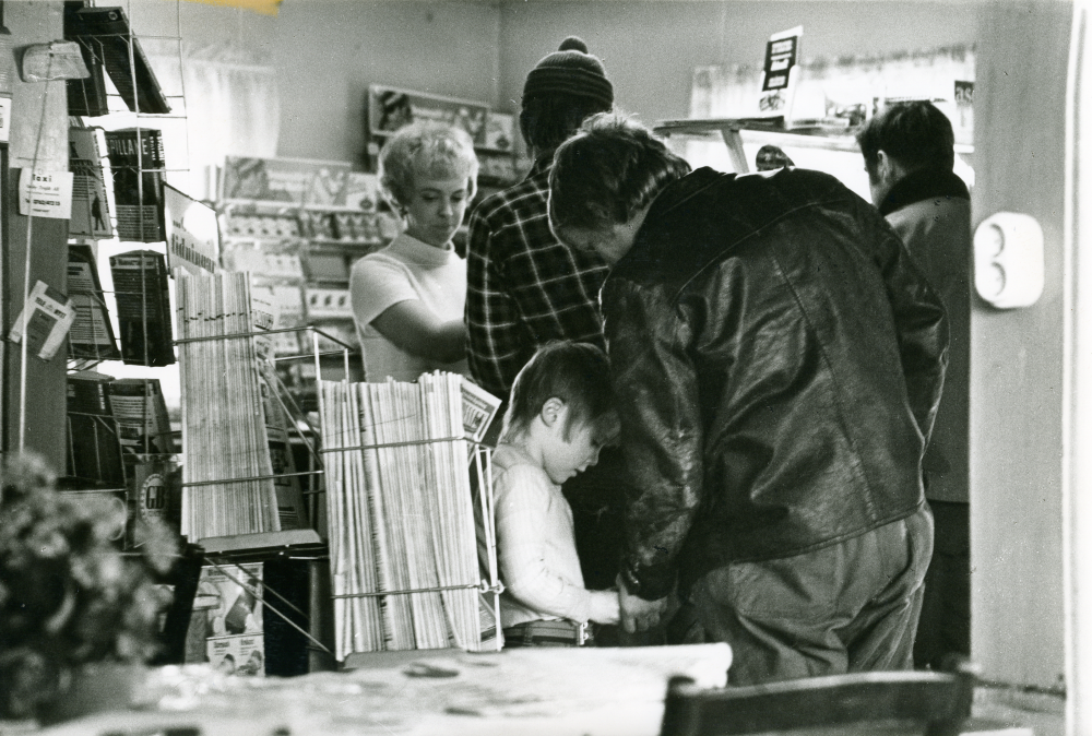 Interiör med kunder i Angarns café. Tidningsställ. Kiosk.

•Fotografiet ingår i bildserien ”Vardagsliv i Vallentuna kommun” av Rachael Gough-Azmier & Gunilla Blomé, Haga Studios HB.