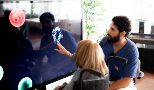 Medarbetare på äldreboende stöttar kund vid digital skärm