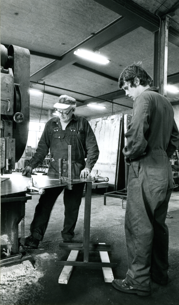 Interiörbild från Danielssons verkstäder den 15:e september 1976. Verksamheten startade 1938 och man tillverkade främst branddörrar och kassaskåp. Under perioden 1964 till 1980 tillverkades dels standardiserade plåtskåp, s. k. kapslingar, för elektriska komponenter, dels specialbeställda plåtskåp. Verksamheten upphörde 2009.
Till vänster står Ingemar Storm. Till höger Gunnar Berg.

Uppgifter: Roslagsbanan och bygden 1885-1985 samt Leif Fredriksson.