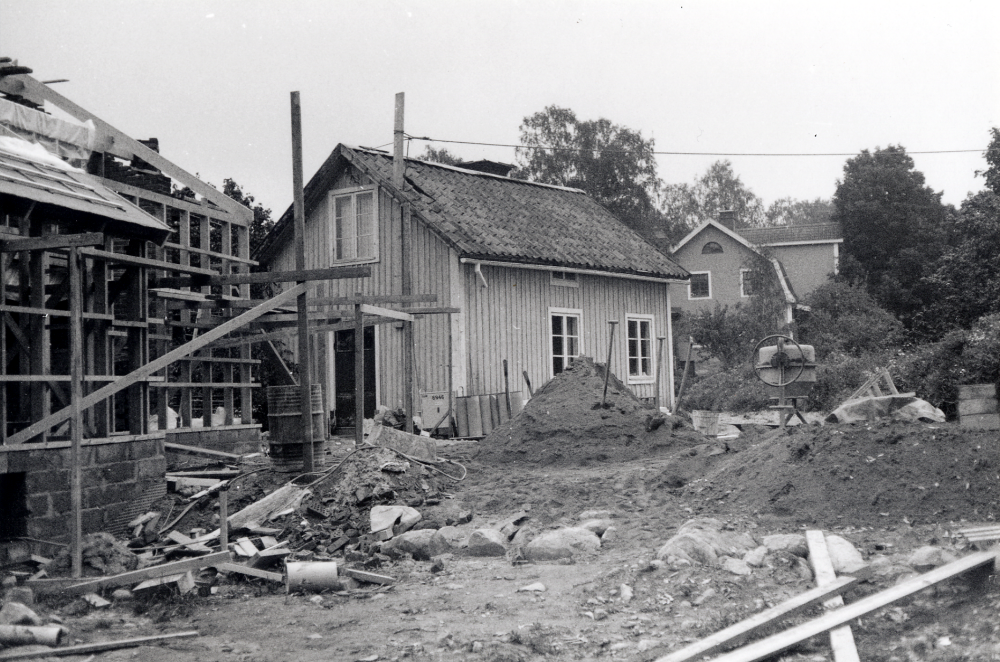 Gammal och ny bebyggelse vid  Skolvägen i  området Trekanten.  Det ljusa huset, f d Halvarssons affär,  kommer att rivas tillsammans med annan äldre bebyggelse när den nya stadsplanen för området förverkligas i mitten av 1980-talet.  Villa Framnäs med brutet tak syns i bakgrunden