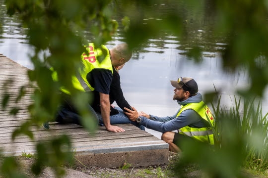 Två Civila insatspersoner hjälper en person som sitter på en brygga.