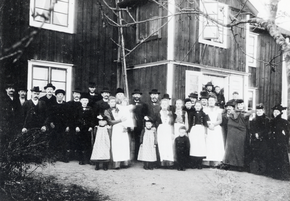 Husförhör på Stolp-Ekeby gård. Fr v nr 8 Jansson, bonde vid Stolp-Ekeby, nr 9 Elsa Gustafsson, nr 11 gårdens matmor Elin Gustafsson med dottern Elvira 'Viran' Gustafsson, gift Österberg, på armen, nr 13 kyrkoherde Carl Maurits Anjou, nr 14 M W Mattsson, arrendator på Frösunda prästgård, nr 15 Ester Gustafsson, nr 19 Fritz Gustafsson, nr 20 fru Gustafsson, barnen G:s farmor, barnpigan Cecilia  kom från Stockholm, nr 24 herr Hill, nr 26 fru Hill, nr 27 Oskar Gustafsson, gårdens brukare, gift med Elin och far till Elsa, Viran, Ester och Fritz, nr 29 fröken Hammarlund, hyrde på Stolp-Ekeby, nr 30 Gunhild Carlsson-Waldebäck, fotografens fru och nr 31 lärarinnan Lisa Barthelsson.  Publicerad i DN runt stan 1984-06-21. Svar med uppgifter från Viran Österberg, barnet som sitter på moderns arm. Viran var 1 år och 18 dagar vid husförhöret. Viran gifte sig med Göte Österberg och flyttade 1937 till Bergs gård  Frösunda.