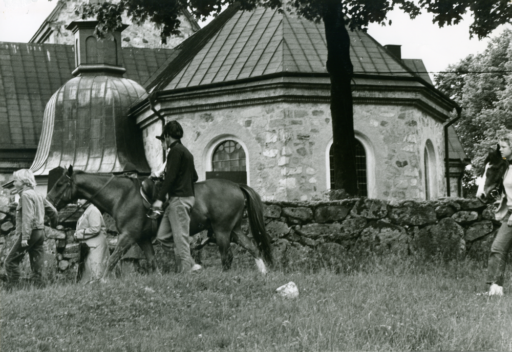 Traditionsenligt midsommarfirande på Kyrkängen i Vallentuna med anordnade ridturer för barnen. Kyrkan i bakgrunden.
•Fotografiet ingår i bildserien ”Vardagsliv i Vallentuna kommun” av Rachael Gough-Azmier & Gunilla Blomé, Haga Studios HB.
