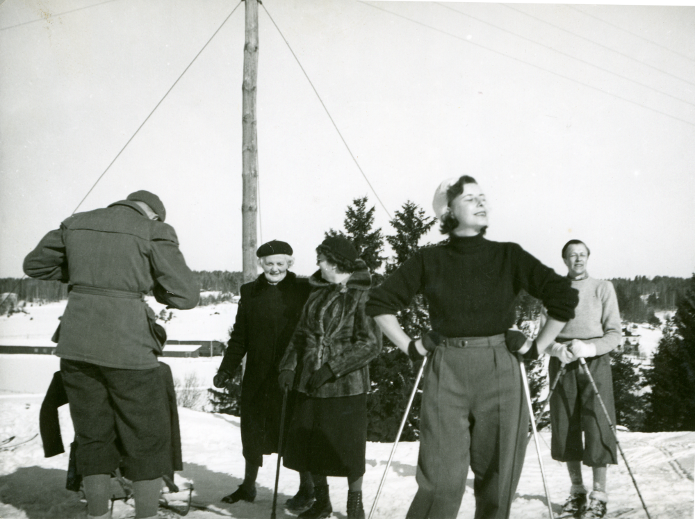 På skidtur vid Ekskogens gård. Från vänster Bertil Sundmark, Inez Ekholm, Vera Sundmark, Britta Sundmark i förgrunden och Bo Sundmark. Familjen Sundmark var sommargäster på Ekskogens gård 1945-1955 och hyrde gårdens övervåning. Nils var hamnkapten och gift med Vera. Deras son Bo var gift med Birgitta. Bilden är tagen vid påsk då familjen Sundmark var på besök. I bakgrunden till vänster skymtar snickerifabriken.