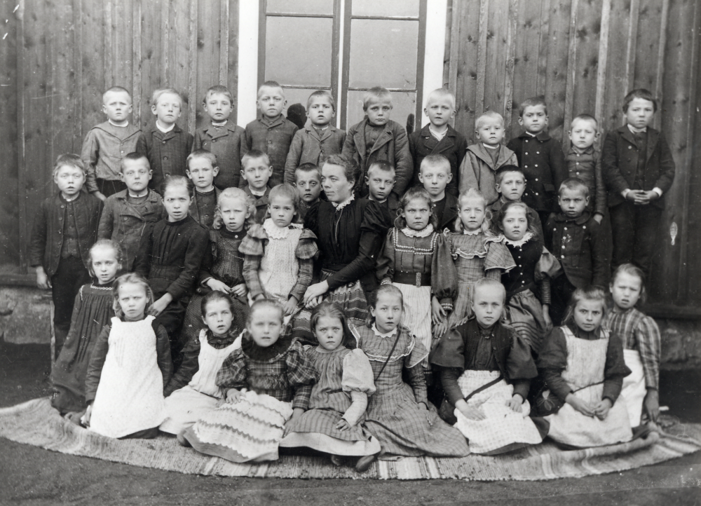 Lärarinnan Maria Nyberg, död 1926, med barnen utanför Kårsta kyrkskola.  Bakre raden fr  v nr 6 är Edvin Scärd, andra raden nr 1 fr v är Anton Jansson.  Flicka nr 1 fr h sittande på en stol är Engla Mattsson, Margit Svärds mamma.  Flcka nr 1 fr v som sitter på marken är Agnes Gustavsson-Wester.  Kan vara från 1897!