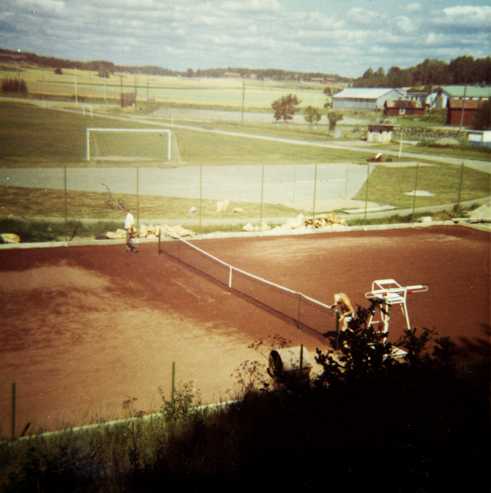 Kårevallen;  Idrottsplatsen Kårevallen i Kårsta. I bakgrunden till höger skymtar Danielssons verkstäder. På bilden syns Bertil Eriksson som byggde tennisplanen och som också var föreningen GoIF Kåres ordförande 1966-1972.