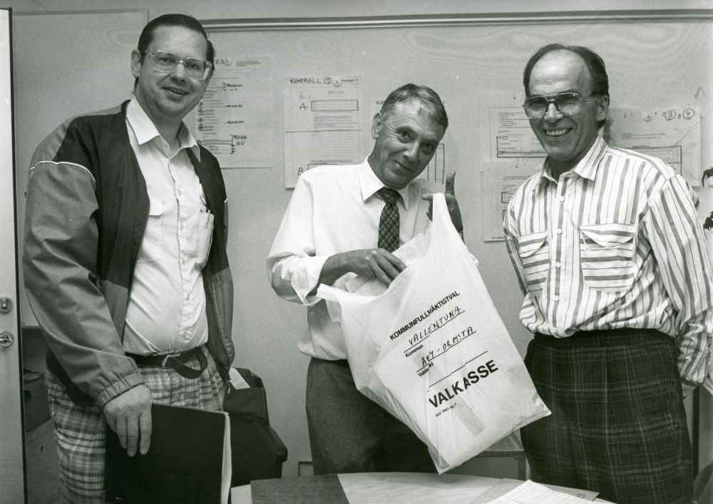 Val 1988. Mannen i mitten håller i en plastkasse märkt "Kommunfullmäktigeval, Kommun Vallentuna, Valdistrikt Åby-Ormsta, Valkasse. Till höger Sven Nyberg (C), Grana gård. Övriga okända.