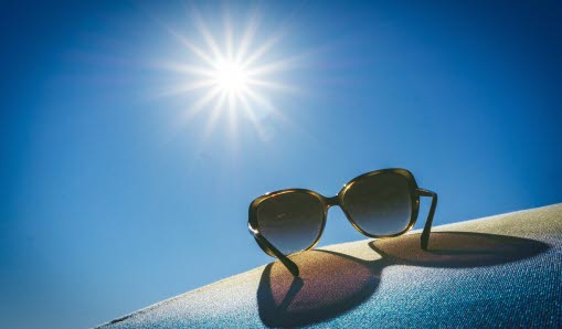 Solglasögon på marken och ovanför skiner solen.