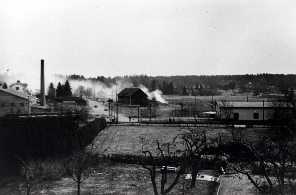 Brinnande halmstackar vid  Åby gård  T v ligger  Vallentuna tegelbruk  och bakom det fabrikör  Axel Lundqvists  villa. Röken skymmer arrendatorsbostaden vid Åby gård.  Tegelbruket är nyuppbyggt efter branden 1946