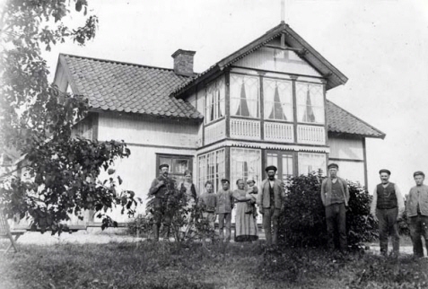 Hus. Framför huset står en grupp människor. 