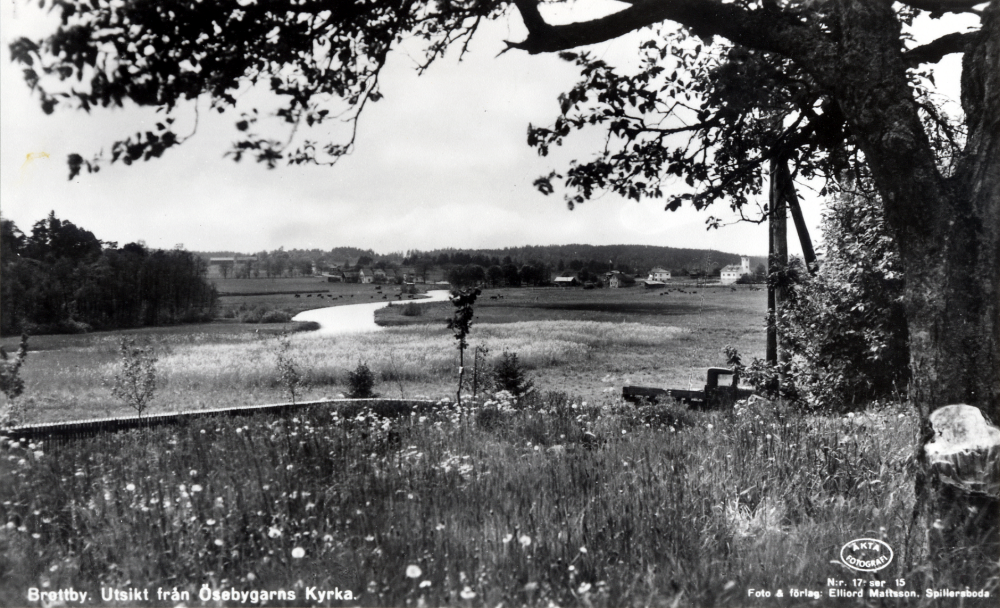 Utsikt från Össeby-Garns kyrka mot Husaåns utlopp.  T h under trädet skymtar i bakgrunden brandstationen.  I förgrunden passerar en lastbil på vägen nedanför kyrkan