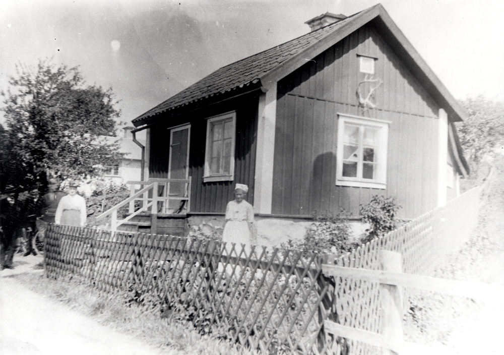 Klockarborg i Lilla Garn.  Utanför huset t h står Olivia Söderberg.  Övriga personer är okända.  I bakgrunden skymtar det vita huset som bröderna byggde och bodde i sedan de växt upp. I det röda huset bodde från början klockarsonen Hjalmar Söderberg och hans hustru Christina Andersdotter.  I stugan födde Christina 10 barn mellan 1876 och 1894, varav ett dog i späd ålder. När båda föräldrarna dött , Christina 1894 och Hjalmar 6 år senare, bodde de fyra sönerna Harald, Nestor, Ragnar och David, som bara var 7 år)  kvar samt den sjukliga systern Jenny.   De äldre flickorna Olivia, Linnea, Alexandra och Genoveva hade alla tagit plaster i familjer eller affärer i Stockholm.  Dottern Olivia flyttade tillbaka till bröderna. De försörjde sig på fiske och diverse arbetsuppgifter på traktens gårdar och var också skickliga att tillverka nät, ryssjor och andra fiskredskap. 1979 avled den siste brodern, Nestor