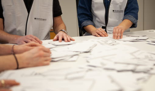 Rösträknare samlade intill ett bord med röstsedlar.