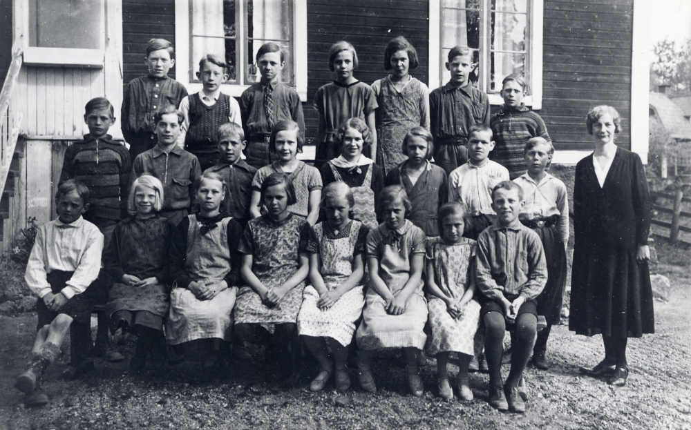 Lärarinnan  Elna Andersson  tillsammans med skolbarnen utanför  Angarns kyrkskola.  Överst fr v:  Bertil Grandin   Henry Eriksson   Erik Johansson   Rakel Axén   Edit Andersson   Tord Johansson-Tordmar. Mittenraden fr v:  Yngve Jansson   Lennart Sjöman   Bayard   Gunnel Johansson   Svea Sjöman   Bayard   Evert Andersson  och  Gösta Johansson.  Nedersta raden:  Knut Sjöman   Majsie Jansson   Astrid Lindersson   Margit Johansson   Astrid Grandin   Ulla Johansson   Aina Lindersson  och  Bertil Jansson
