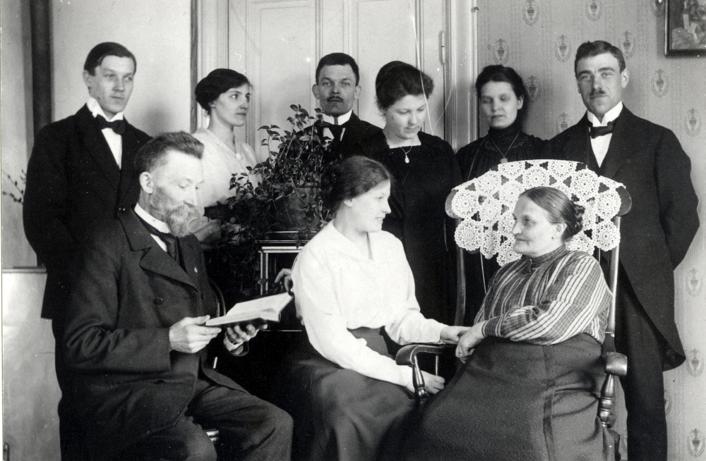 Skomakare K P Gustafsson bodde med sin familj på Allévägen 8. I huset fanns en telefonväxel som dottern Ruth förestod. Familjen hade 11 barn, Hildegard dog 1912.  Här sitter K P, som levde 1841-1941, med hustrun Hilda i gungstolen samt några av barnen.  Hilda levde 1866-1920. I övre raden fr v Cyrus, Beda, Fritiof som hade skomakaeri på Banvägen, Jenny och Ester  samt Esters fästman Reinhold Rejnegård.  Mellan föräldrarna sitter Anna.  K P läser i en bok - psalmbok - bibel????