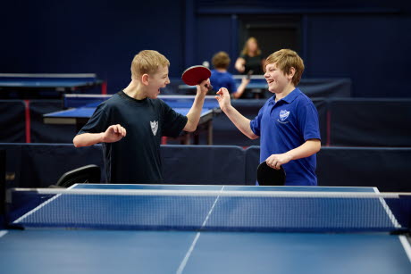 Två killar som står på samma sida om ett bordtennisbord.