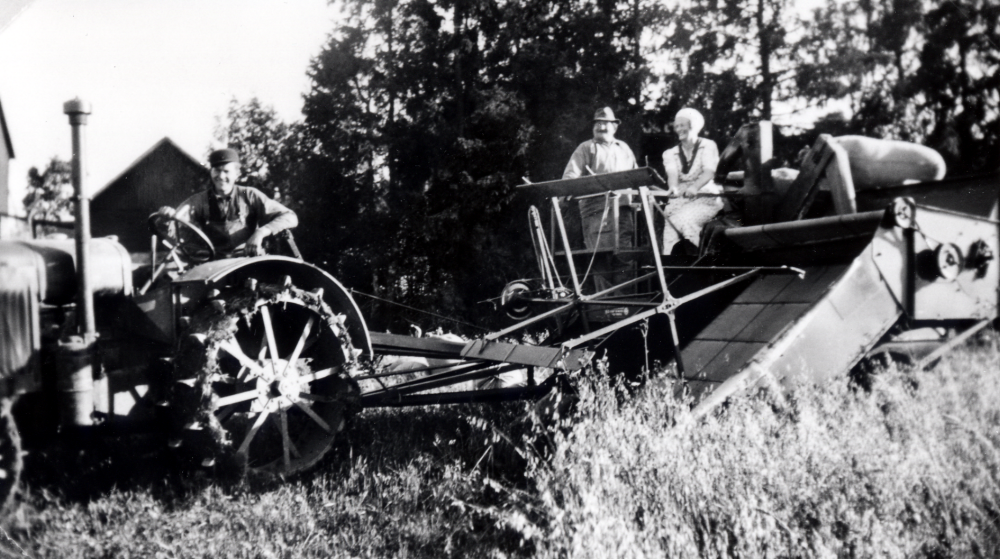 Inez och Manfred Ekholm flyttade 1947 till Ekskogens gård i Kårsta. Dessförinnan hade de bl a Jällsta gård i Skyttorp. Här skördas havren på Jällsta med skördetröska, Erik Eriksson kör traktorn, Adolf Persson knyter ihop säckarna och Inez Ekholm sitter på tröskan