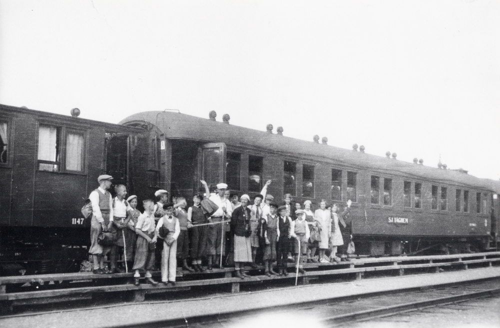 Elever från Hjälmstaskolan på skolresa  till Jämtland. Här står alla utanför SJ tåghem (i Östersund eller Åre?).  Läraren Josef Andersson och en kvinna (Margareta Andersson?) står tillsammans med barnen på perrongen