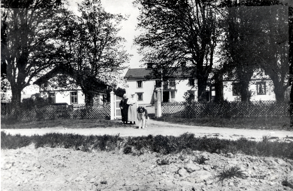 Väsby gård i Vallentuna.  Framför grinden står Johanna Carlsson, hustru till B C Carlsson som köpte gården 1906, och en av parets döttrar, ev Jenny.  Vid västra flygeln hade man bikupor.  I familjen fanns oftast också en Sankt Bernhardshund,  som alltid gick lös och som någon gång gav sig ut på jakt på grannarnas får