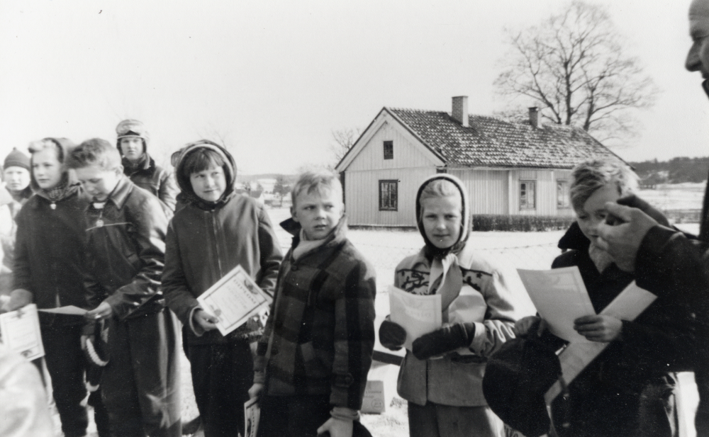 Nils Alstermark delar ut diplom på skolgården till skolbarnen i Vada skola läsåret 1956-57.  Fr v står Jan-Olov Grönborg, Åsa Ahlgren, Kurt Andersson, Bengt Nilsson Arken, Anita Andersson(Wallin), Nils Jansson, Ingrid Grönborg, Börje Johansson och prisutdelaren Nils Alstermark.  Det är snö på marken – skidtävling?