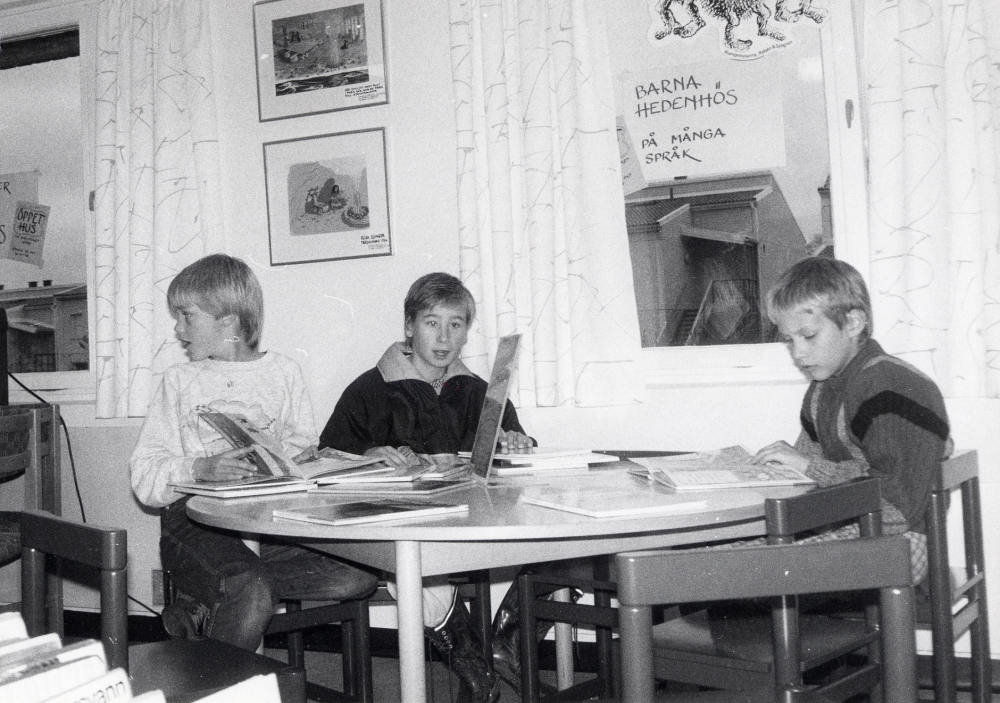 Karby bibliotek har reparerats sommaren 1987 och invigs med öppet hus 25 oktober. I nya barn- och ungdomsavdelningen sitter fr v Camilla Sjögren, Niklas Pettersson och Ulf Trädgårdh och tittar i Bertil Almqvists böcker om Barna Hedenhös på olika språk