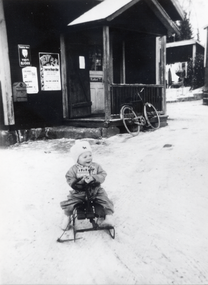 Hulda Maria Eriksson  och Gösta Eriksson  övertog  Sursta handel  1944. Nytt affärshus bygdes 1955 och var i drift till 1963. I affären fanns 1955-1975 en biblioteksfilial, vilken också sköttes av makarna Eriksson. Här sitter Erikssons son  Christer Eriksson  på en  kälke  utanför gamla affären. Observera  affischerna  vid ingången.  Se Lanthandlare i vallentunasocknarna vid Roslagsbanan.