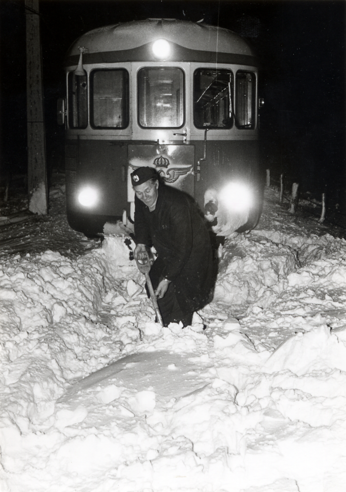 En dieseldriven rälsbuss  har kört fast i snön strax före Ekskogens järnvägsstation. Föraren Erland Svärling har gått ut för att skotta banan fri.