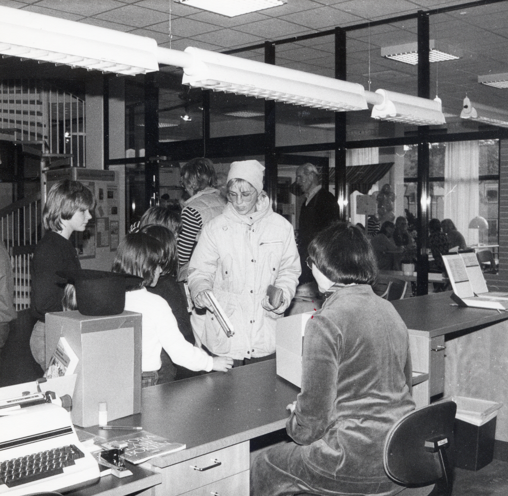 När svenska tryckerikonsten firade 500-års jubileum hade biblioteket öppet söndagen den 9 oktober med utlåning, program och utställningar. Här sitter Margareta Dethorey med ryggen mot kameran i låneexpeditionen i Vallentuna bibliotek och stämplar ut boklån med hjälp av kamera
