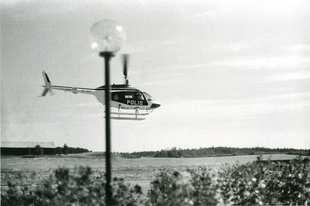 En polishelikopter lyfter över Brottbys åkrar en sommareftermiddag.
•Fotografiet ingår i bildserien ”Vardagsliv i Vallentuna kommun” av Rachael Gough-Azmier & Gunilla Blomé, Haga Studios HB.