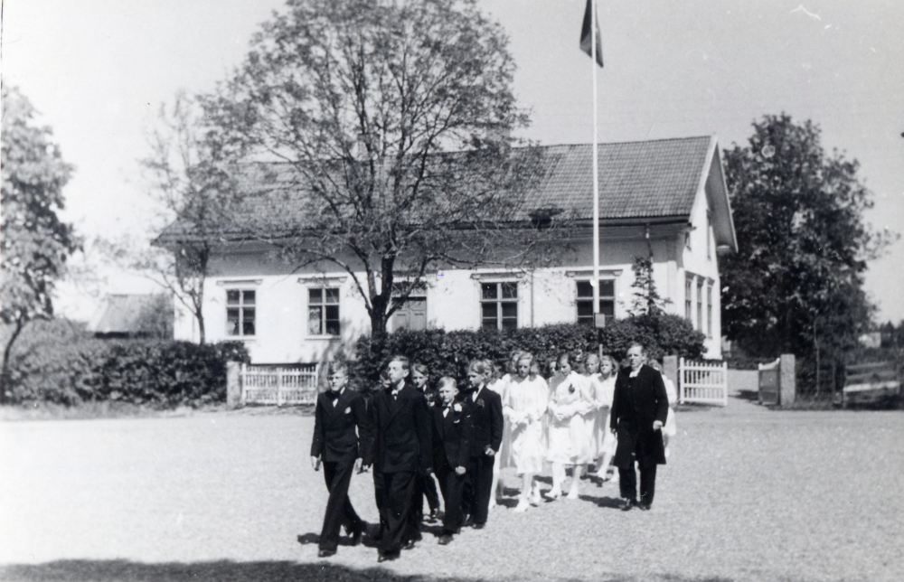 Kontraktsprost Sven Vängby lämnar Klockargården tillsammans med sina konfirmander för konfirmation i Vallentuna kyrka. Stämplad på baksida: Vallentuna skolexp 29 juli 1964