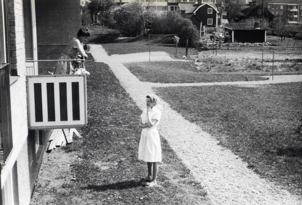 Vy från baksidan av Enebackens gula fasadtegelhus vid Fornminnesvägen mot Mörbyvägen.  I bakgrunden syns de röda tegelhusen Rickebyhöjd  längs Mörbyvägen.  Det röda huset  med vita knutar tillhör Lars Lasse Johanssons ("Sop-Johan") föräldrar.