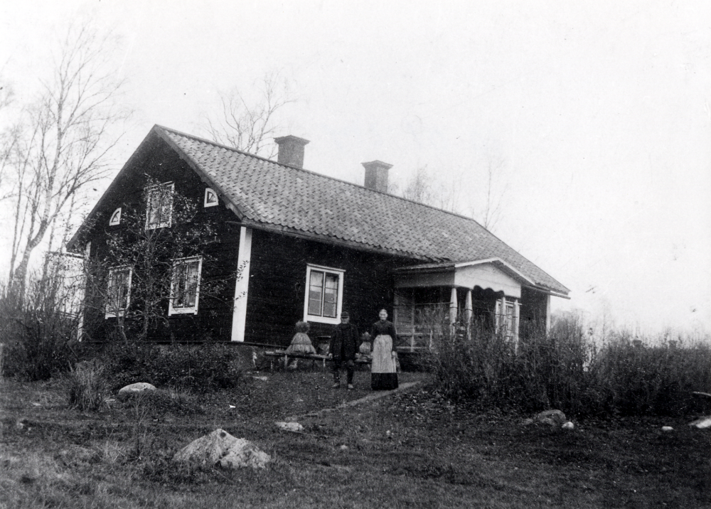 Lilla Seneby i Vada. T v utanför boningshuset står Johan Axelsson, född 13 juni 1826 i Vada och död i Vada 3 juni 1905. Bredvid står hustrun Kristina Sofia, född Arrhén. Hon föddes i Östra Ryd 7 maj 1829 och dog i Vada 5 januari 1905. Vid huset står bikupor av halm