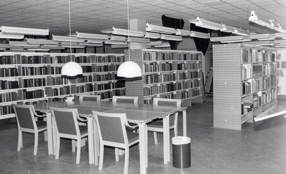 Interiör från Vallentuna bibliotek. I förgrunden läsplatsen vid referenshyllan, vars skjutbord skymtas t h.  I taket hänger schalar