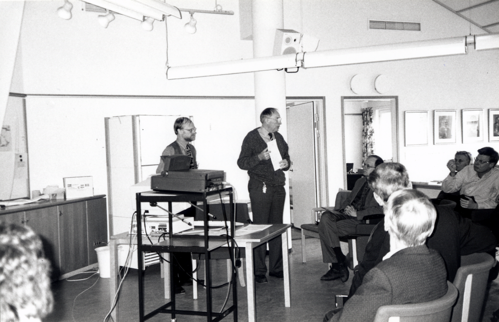 Vallentuna folkrörelsearkiv har studiedag i Bällstarummet, Vallentuna kommunalhus. Ordförande Uno Sköld hälsar välkommen och arkivarie Urban Johansson från stadsarkivet i Norrtälje står t v.  Bland åhörarna sitter i första raden fr h Karl-Erik Nilson och Fred Berglund, rad 2 fr v Ingrid Ullman och Hans Hällgren